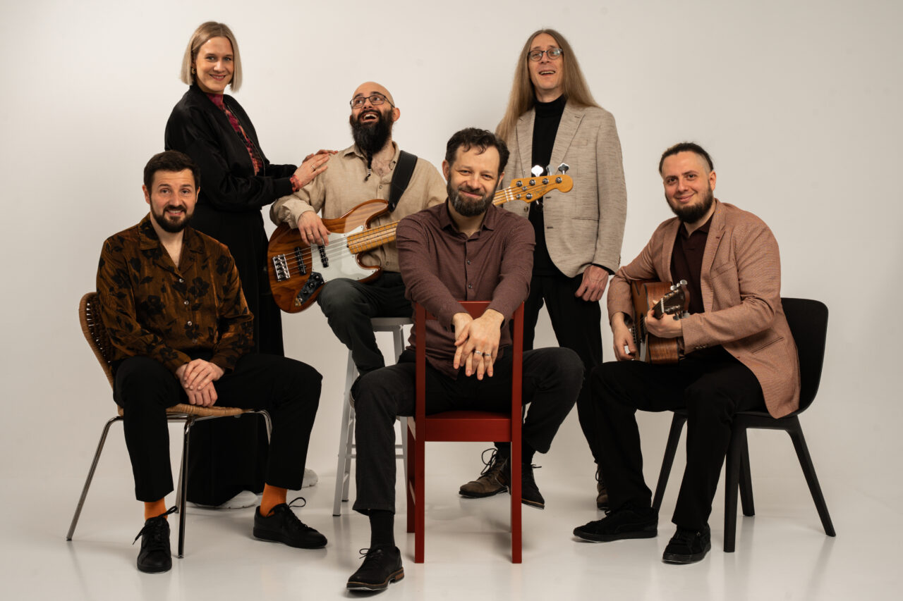 Studio-Gruppenporträt der sechsköpfigen Band Picked Up mit Instrumenten vor hellem Hintergrund.