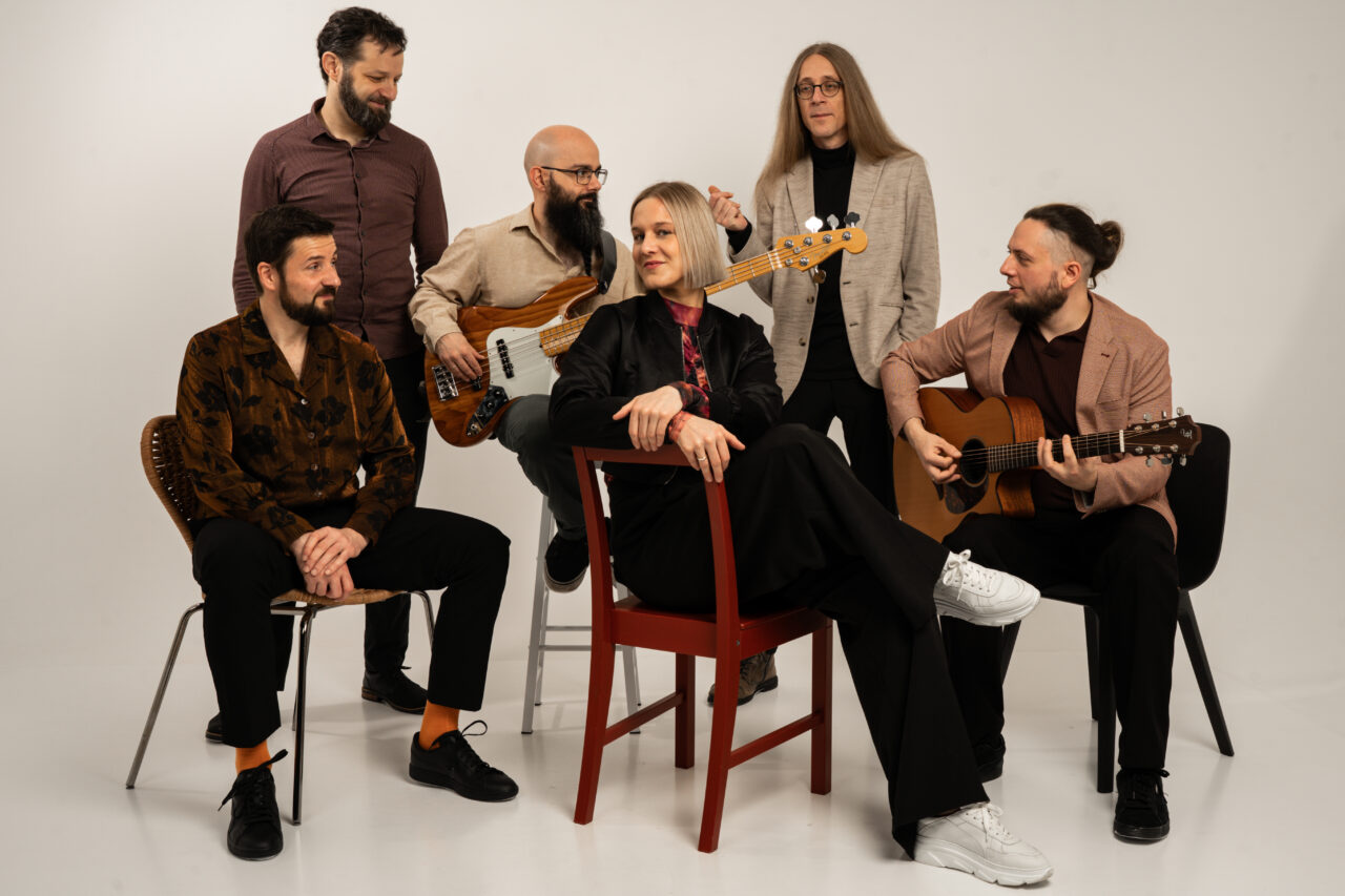 Studio-Gruppenporträt der sechsköpfigen Band Picked Up mit Instrumenten vor hellem Hintergrund.