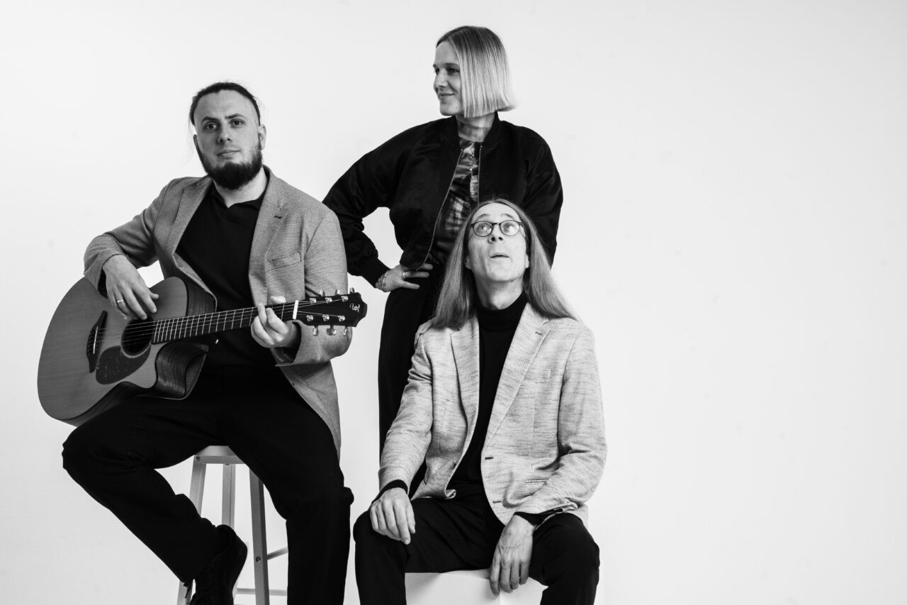 Studio-Gruppenporträt der Band Picked Up mit Instrumenten vor hellem Hintergrund.