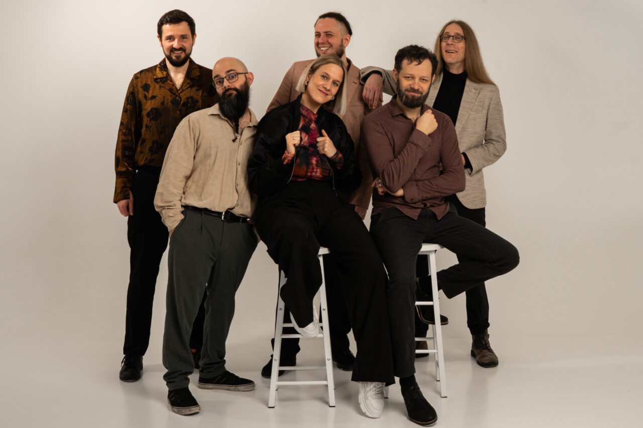 Studio-Gruppenporträt der sechsköpfigen Band Picked Up mit Instrumenten vor hellem Hintergrund.