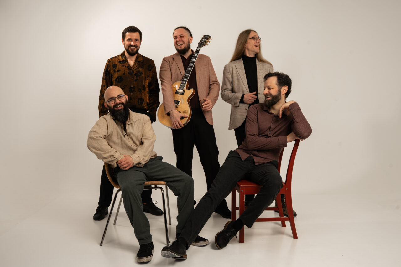 Studio-Gruppenporträt der Band Picked Up mit Instrumenten vor hellem Hintergrund.